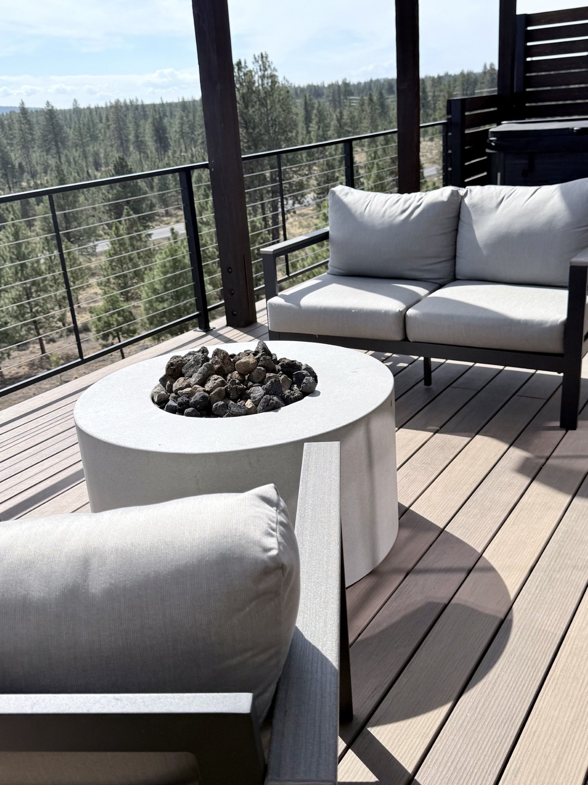 A deck with a round table, two sofas, and a fire pit.