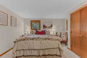 A bedroom with a large bed, two bedside tables, a chair, a wooden wardrobe, and framed artwork on the walls. - Cozy Condo at Waterville Estates (Thornton)
