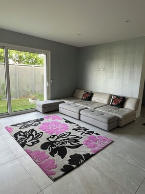 Un salon moderne avec un canapé d’angle, une grande porte-fenêtre coulissante et un tapis à motifs.