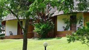 Un edificio con techo de paja, un césped, un árbol y un objeto esférico en un asta.