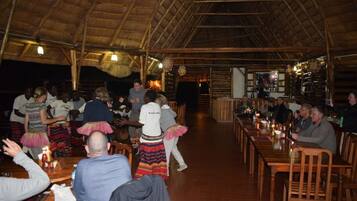 A restaurant with wooden tables and chairs, a thatched roof, and a bar area.