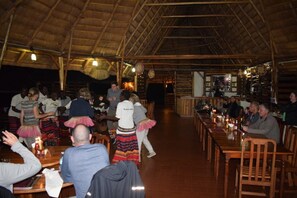 Un restaurante con mesas y sillas de madera, techo de paja y una zona de bar.