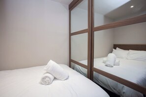 Ein Hotelzimmer mit einem großen Spiegel, der das Bett reflektiert, und einem ordentlich bezogenen Bett mit aufgerollten Handtüchern.