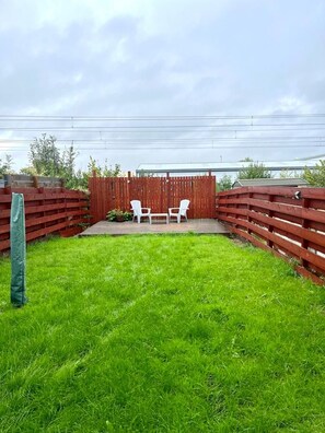 Ein Garten mit Holzzaun, zwei weißen Stühlen und einem Rasen.