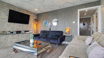 Una sala de estar moderna con un televisor de pantalla plana, un sofá azul oscuro, una mesa de centro de vidrio y una pared gris con textura.
