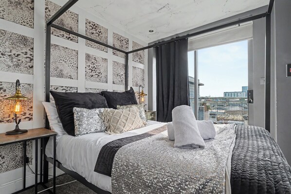 A modern bedroom with a large bed, a city view, and a patterned wall.