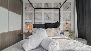 Een moderne slaapkamer met een hoofdbord met een geometrisch patroon, een groot bed met witte handdoeken, twee bedlampjes en een nachtkastje met een decoratief object.