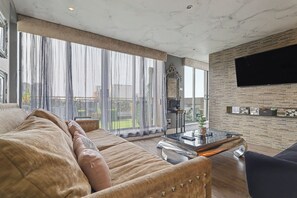 A spacious living room with a large sofa, a coffee table, and a TV mounted on a brick wall.