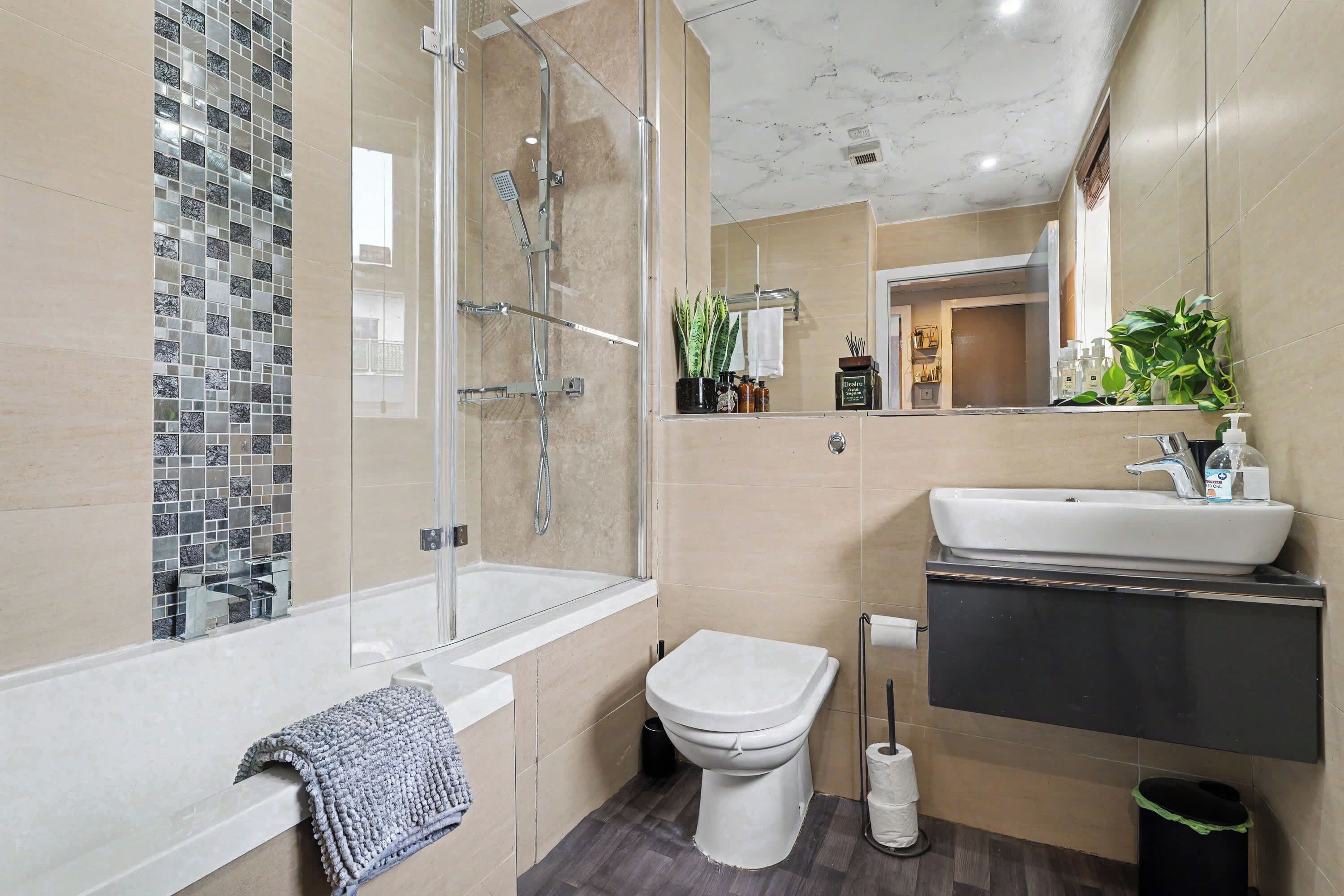 Un baño moderno con ducha envuelta en vidrio, inodoro blanco y lavabo con espejo arriba.