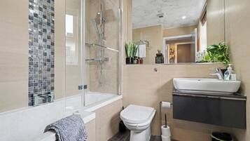 Un baño moderno con ducha envuelta en vidrio, inodoro blanco y lavabo con espejo arriba.
