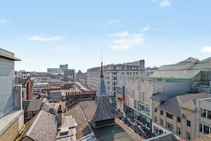 Un paisaje urbano con un campanario de iglesia destacado, edificios históricos y un moderno edificio con fachada de vidrio.