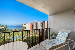 Ein Balkon mit Blick auf einen Swimmingpool und den Ozean, ein Stuhl und ein kleiner Tisch.