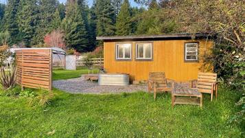 A wooden cabin with a small patio area, a hot tub, and outdoor seating.