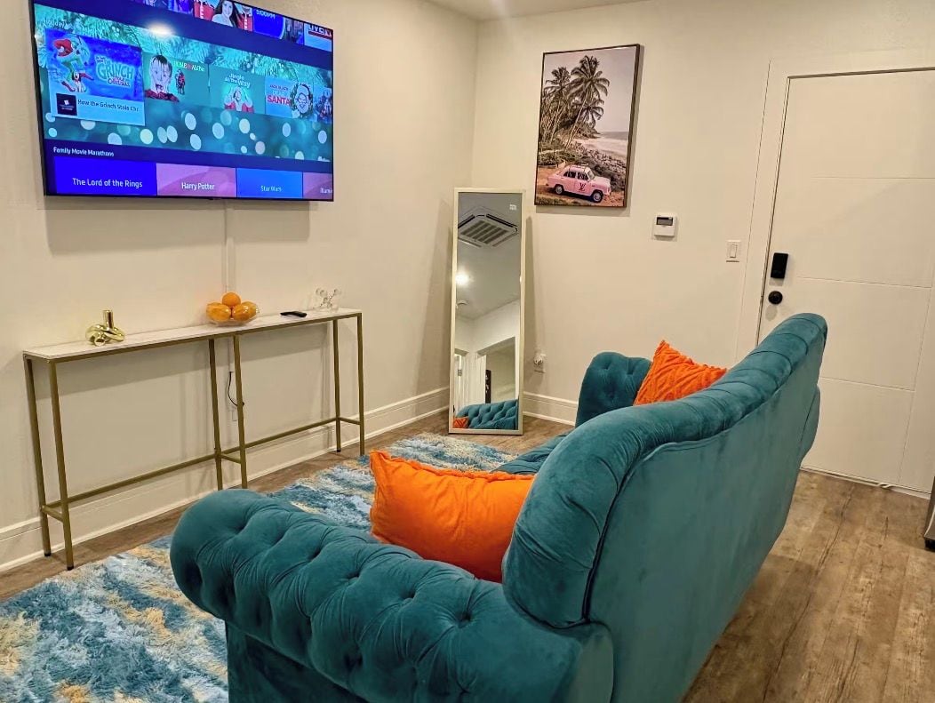 A living room with a teal sofa, a flat-screen TV, a console table, and a mirror.