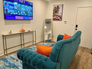 Un salon avec un canapé de couleur turquoise, un téléviseur à écran plat, une console et un miroir.