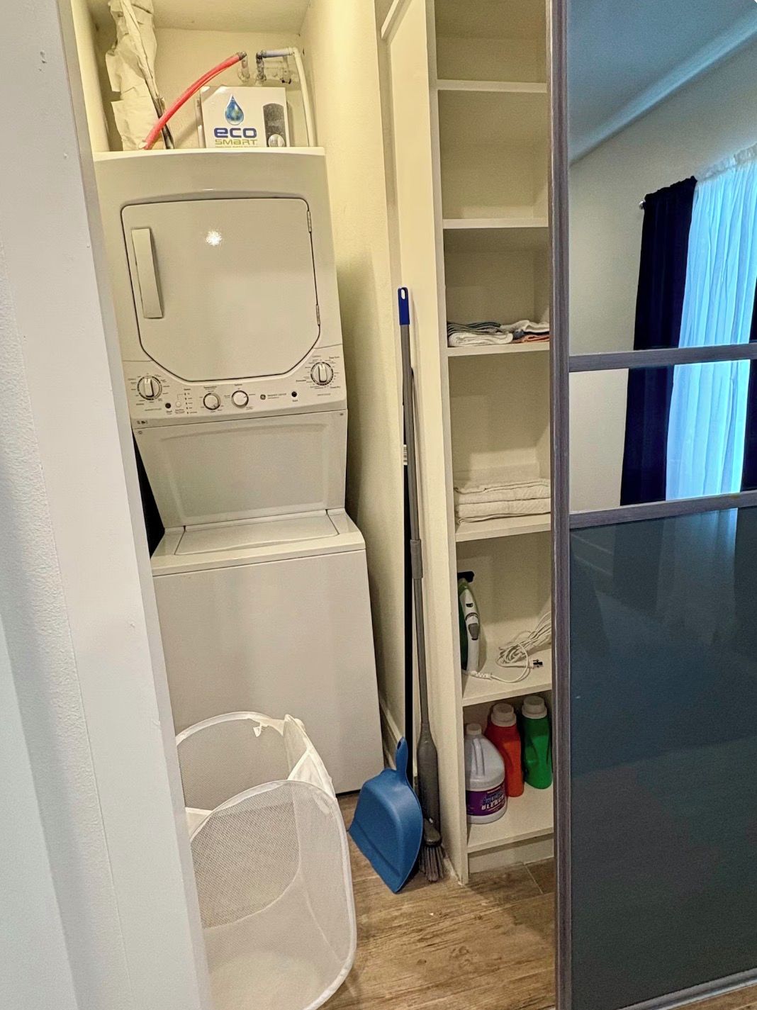 A laundry area with a washing machine, a drying rack, and storage shelves with cleaning supplies.