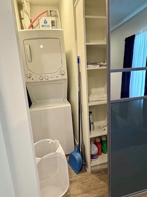 Un espace buanderie comprenant un lave-linge, un étendoir et des étagères de rangement pour les produits de nettoyage.
