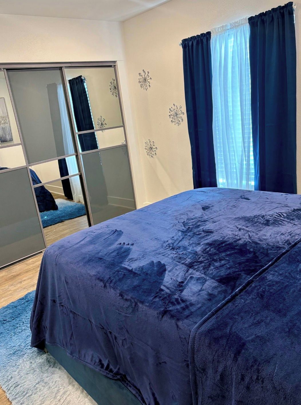 A bedroom with a large bed, a wardrobe with mirrors, and a window with curtains.