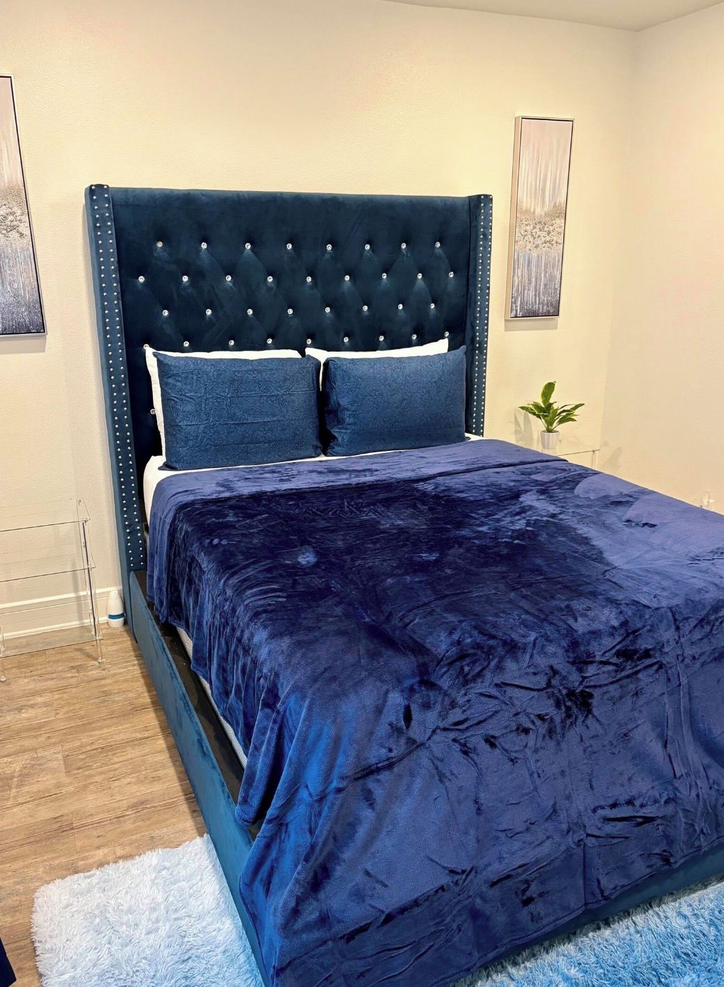 A bedroom with a tufted headboard, a dark blue bedspread, and a white fluffy rug.