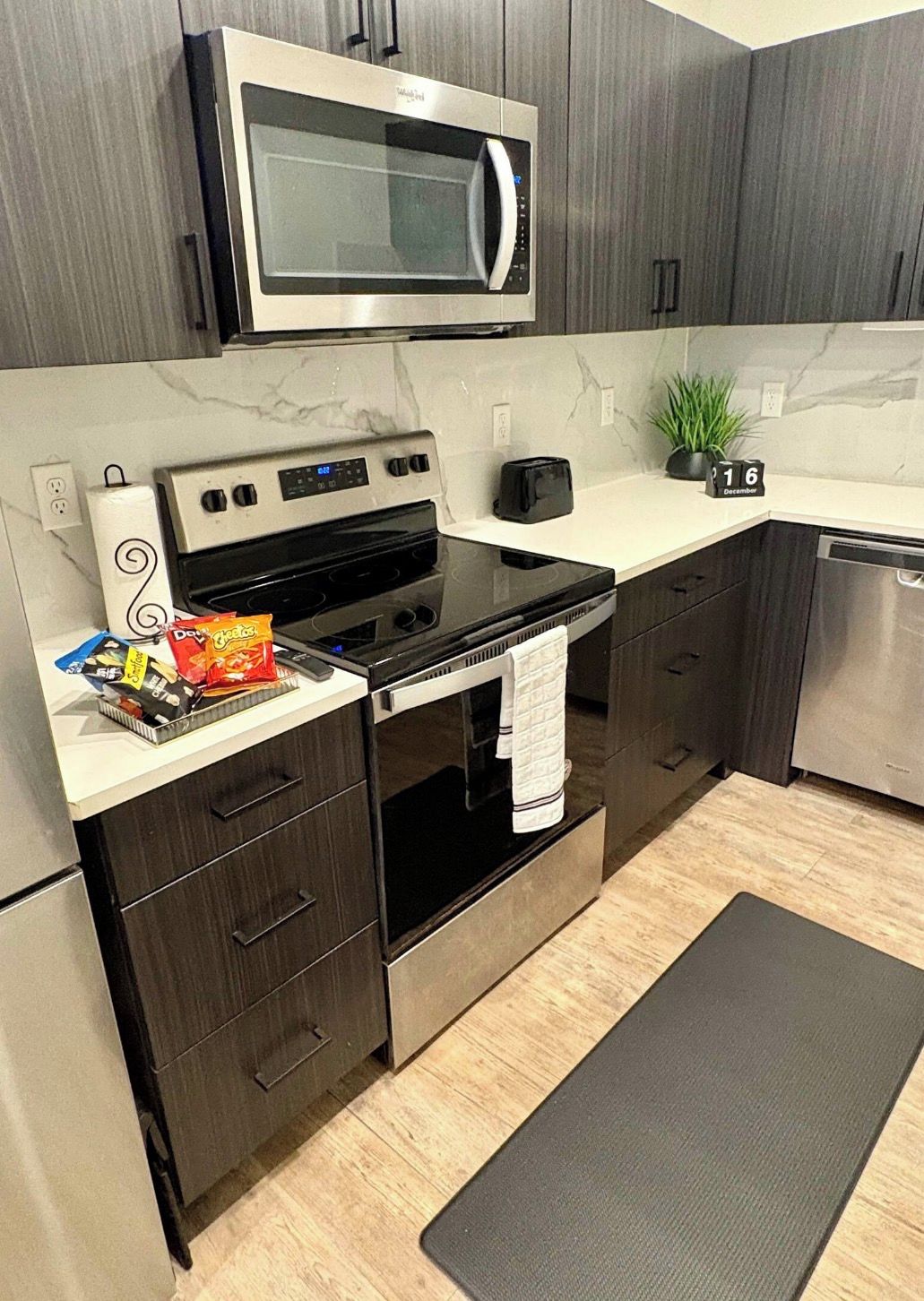A modern kitchen with dark cabinetry, a stainless steel microwave, a stove, and a toaster.