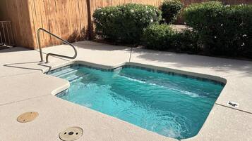 A swimming pool with a wooden fence, a metal ladder, and a paved deck.