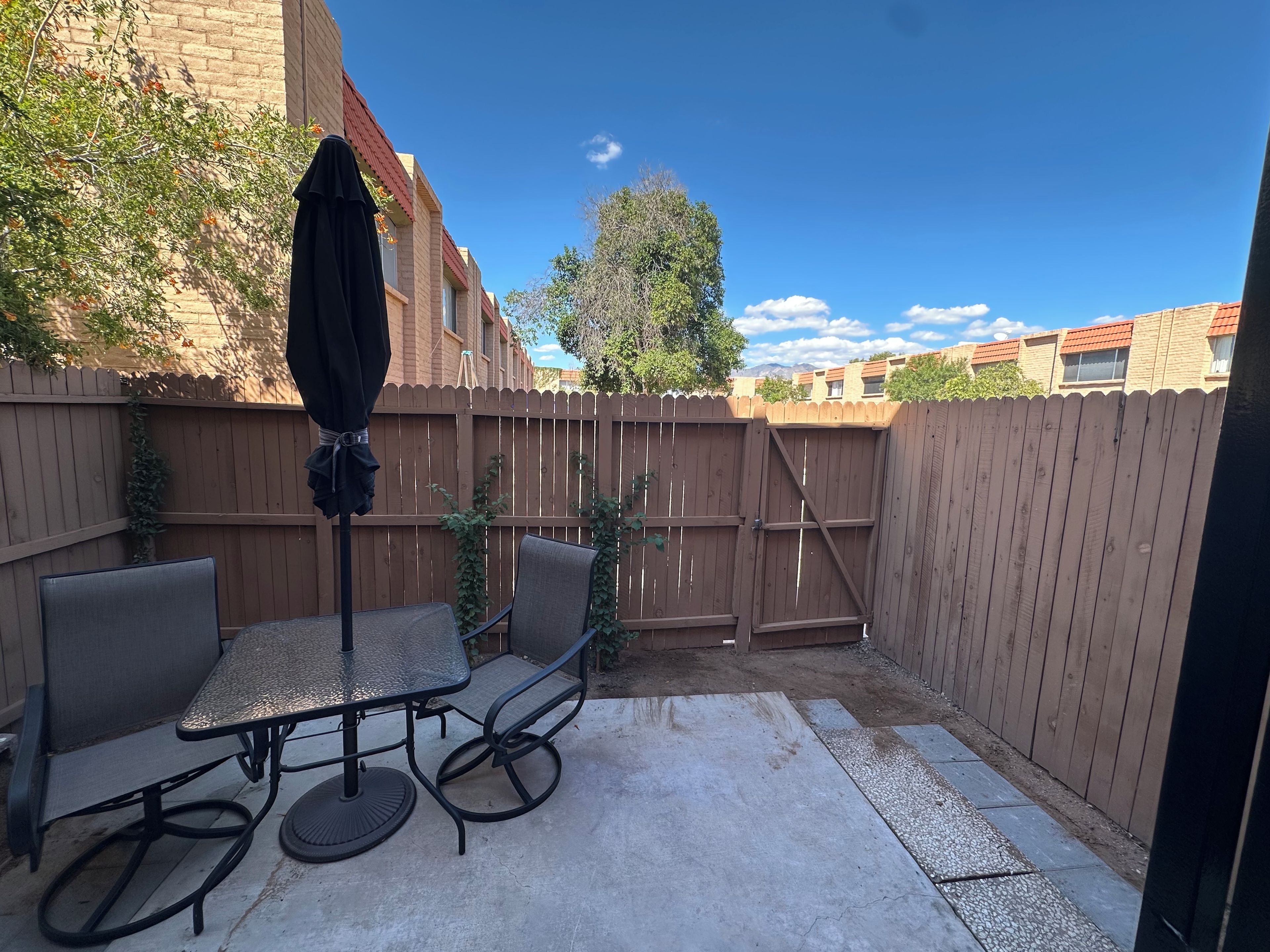 An outdoor patio area with a table and chairs, a wooden fence, and a view of neighboring buildings.
