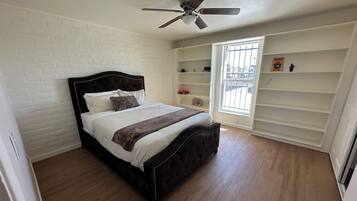 A bedroom with a bed, a ceiling fan, a window with bars, and a white brick wall.