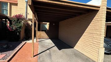 A covered parking area with a brick wall and a wooden roof structure.