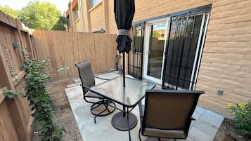 A patio with a table and chairs, a sliding glass door, and a wooden fence.