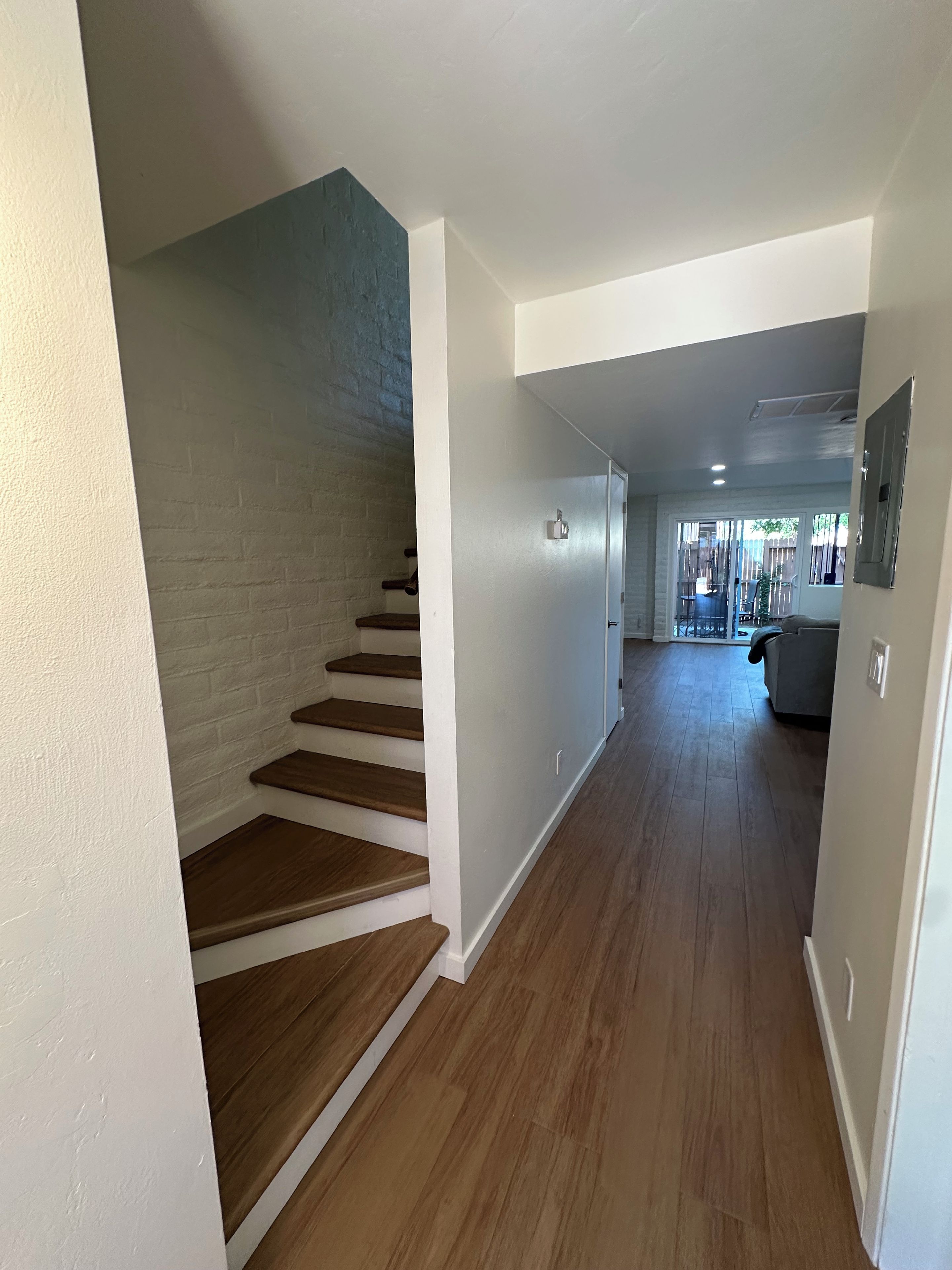 A hallway with wooden flooring and white walls, leading to a living area with a couch and a table.