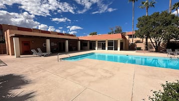 A swimming pool with lounge chairs, a covered patio area, and palm trees.
