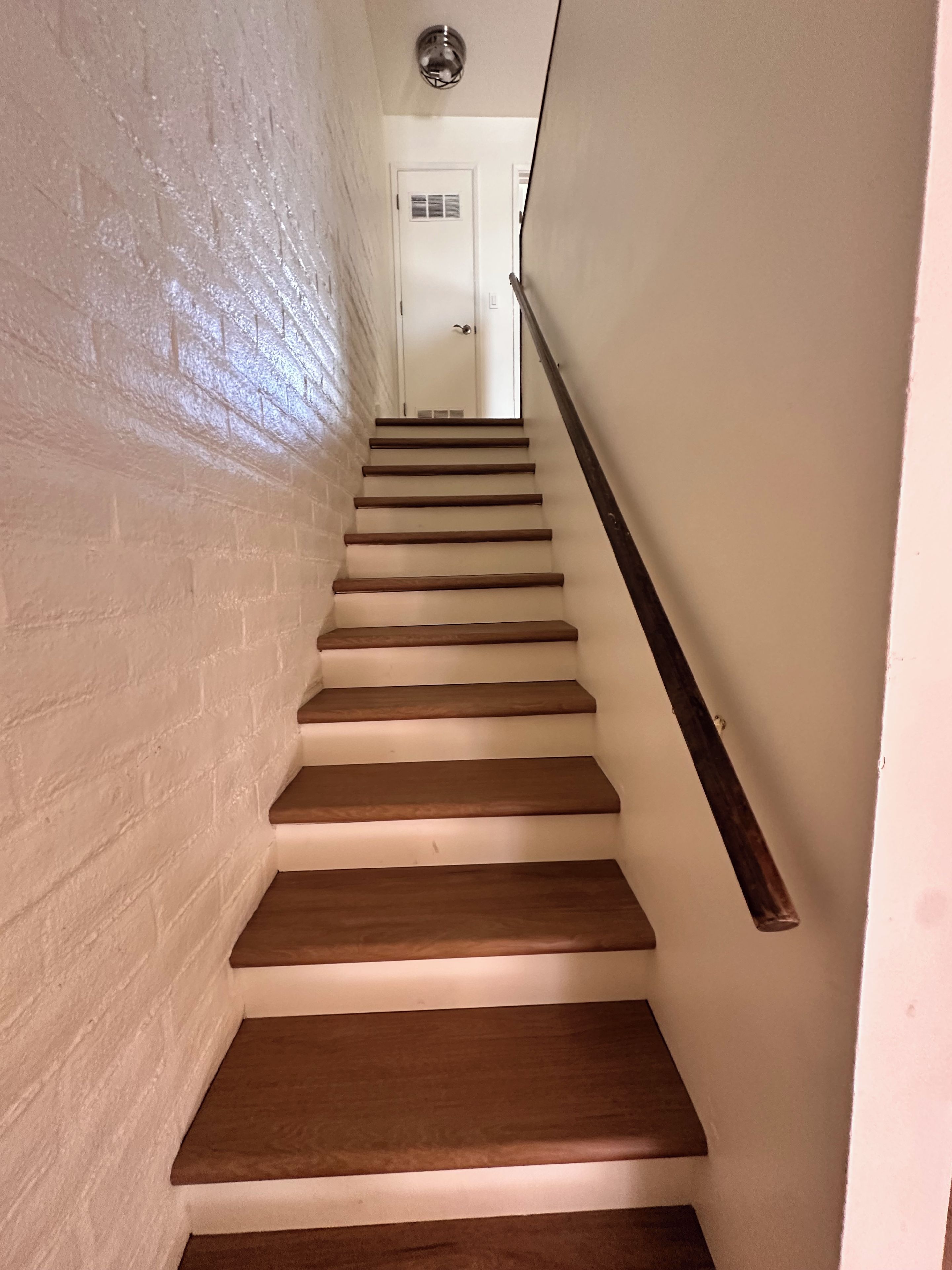 A staircase with wooden steps and a handrail, leading to a door with a window.