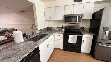 A modern kitchen with white cabinets, a stainless steel refrigerator, a microwave, and a dishwasher.
