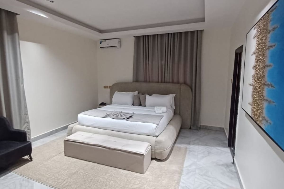 Une chambre d’hôtel avec un lit, une chaise, un tableau et un appareil de climatisation.