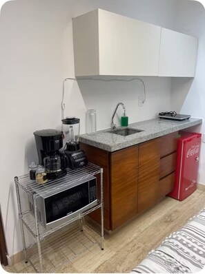 Eine kompakte Küchenzeile mit Kaffeemaschine, Mixer und kleinem Kühlschrank.