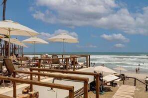 Eine Strandlounge mit mehreren Sonnenschirmen, Liegestühlen und einem Holzdeck mit Blick auf den Ozean.