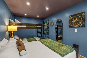 Ein Zimmer mit einem Etagenbett, einer Nachttischlampe, einer grünen Tagesdecke und einem Wandbild.