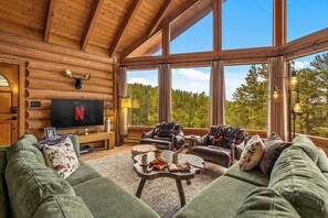 En mysig stuga med en inredd interiör, ett bekvämt vardagsrum, en platt-TV och ett stort fönster med utsikt över skogen.