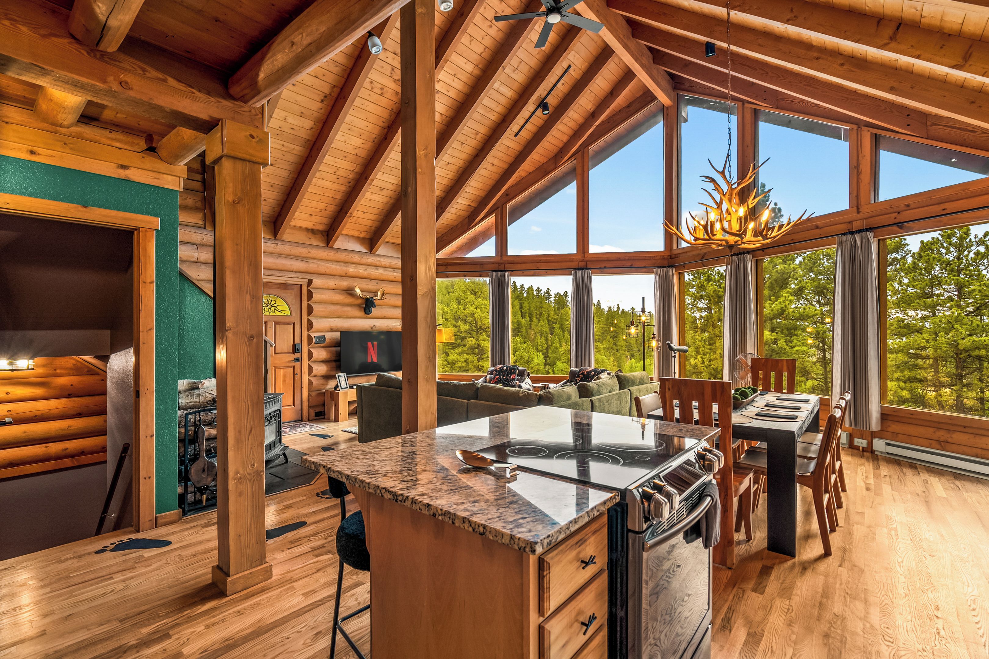 A spacious log cabin interior with a large kitchen island, dining area, and a cozy living space with a fireplace.
