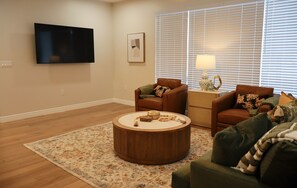 A living room with a flat-screen TV mounted on the wall, a round wooden coffee table, two brown leather armchairs, a green sofa, and a patterned area rug. - 3-bedroom house in delightful Albuquerque Watch the Balloon Fiesta  on the porch (Albuquerque)