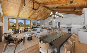A spacious living area with a large dining table, a kitchen, and a view of the outdoors. - The Brush Creek Lookout - Home Away From Home (Crested Butte)