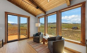 A spacious room with large windows, a wooden ceiling, and a view of a rural landscape. - The Brush Creek Lookout - Home Away From Home (Crested Butte)