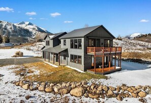 Una casa moderna de dos pisos con balcón, con montañas nevadas al fondo.