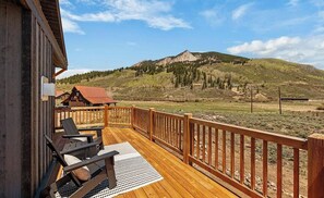 Eine Holzterrasse mit Blick auf einen Berg, ein kleines Gebäude und einen Stuhl.