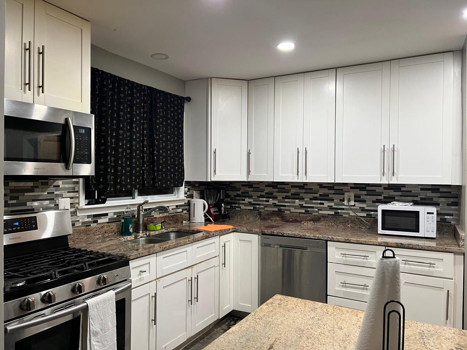 A modern kitchen with white cabinets, stainless steel appliances, and a tiled backsplash.