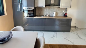 A modern kitchen with a built-in oven, microwave, and a coffee machine on the counter. - Apartments Sava (Tivat)
