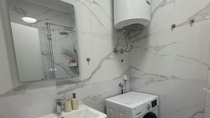 A modern bathroom with a sink, mirror, shower, and a washing machine. - Apartments Sava (Tivat)