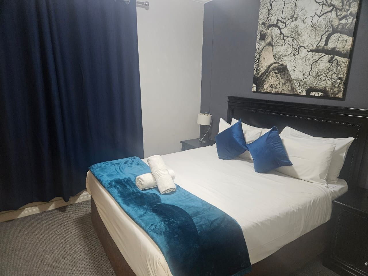 Et hotelværelse med en seng, et natbord, en lampe og et billede på væggen.