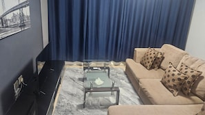 En stue med sofa, dekorative puder, et sofabord i glas og et fjernsyn.