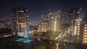 Vista nocturna de un complejo hotelero con varios edificios altos, una piscina e iluminadas calles.